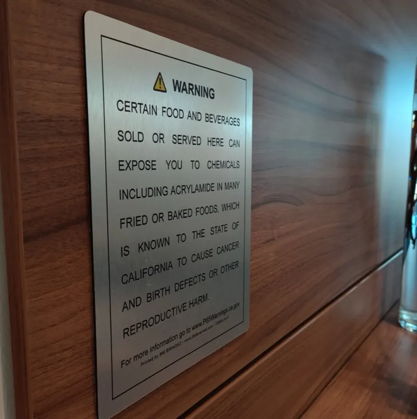 Prop 65 food and beverage warning on brushed aluminum mounted on a wood wall